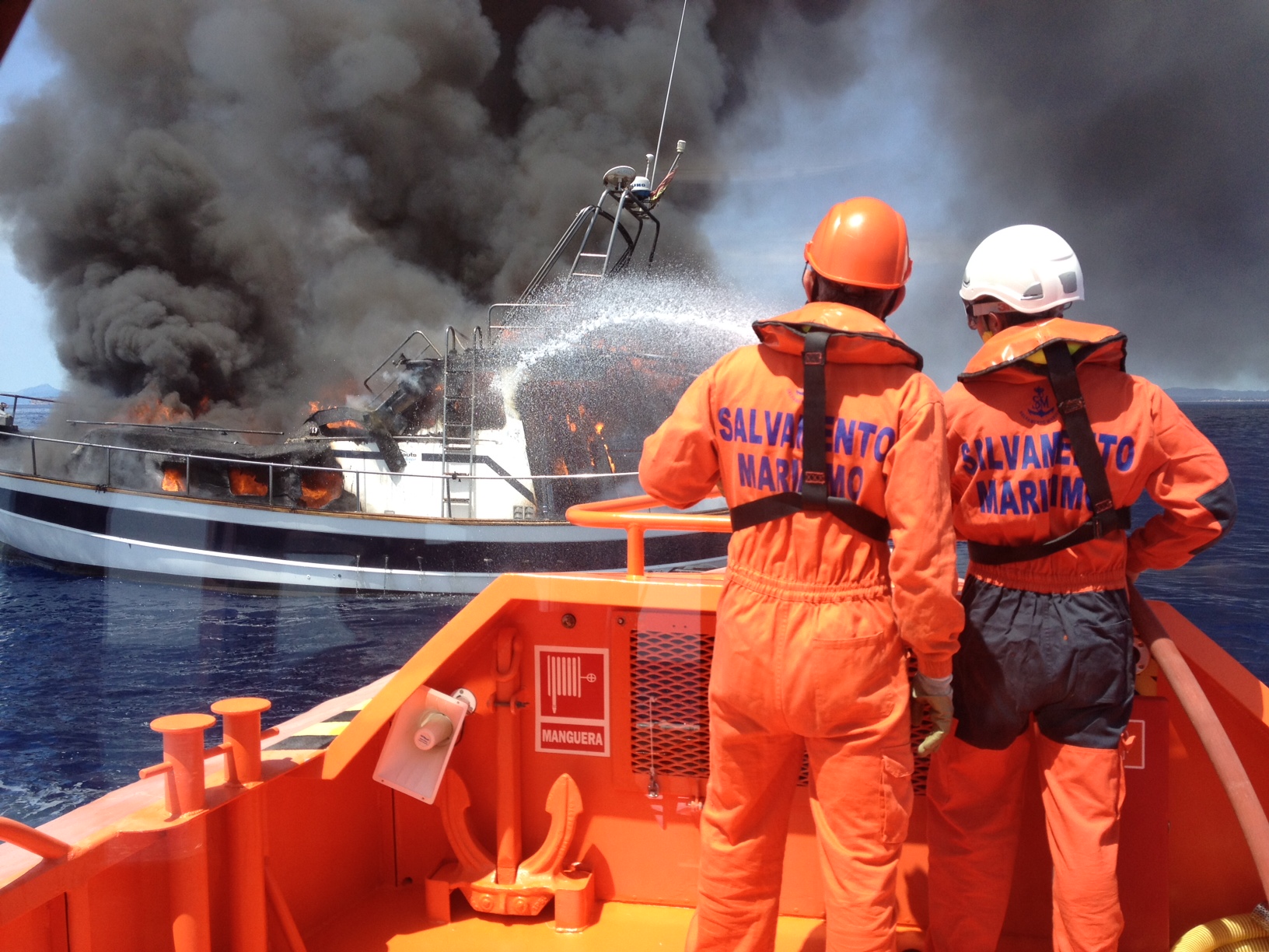 Dos tripulantes de sasemar apagando el incendio de la embarcación