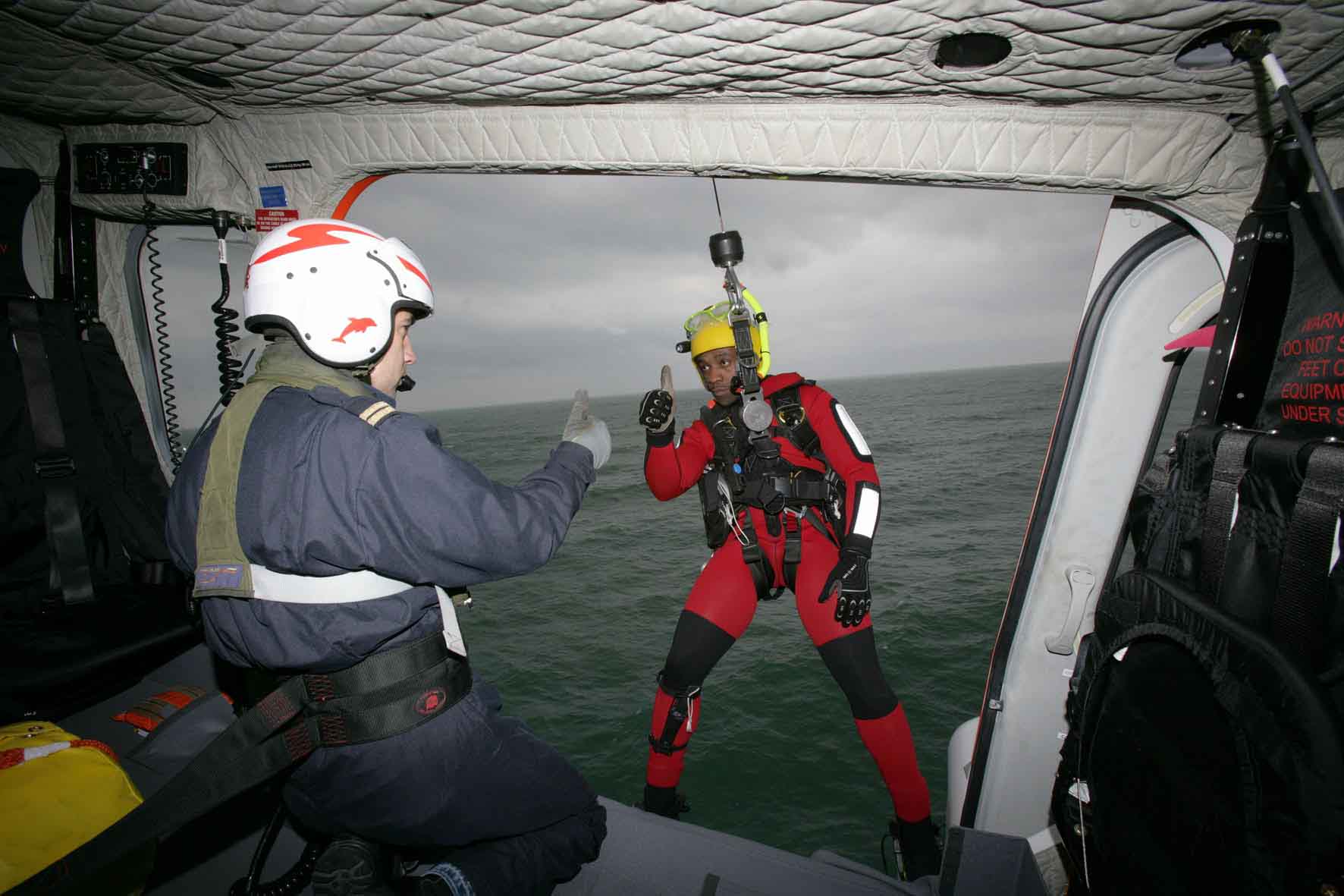 Tripulante helicóptero dando indicaciones a rescatador antes de bajar al mar