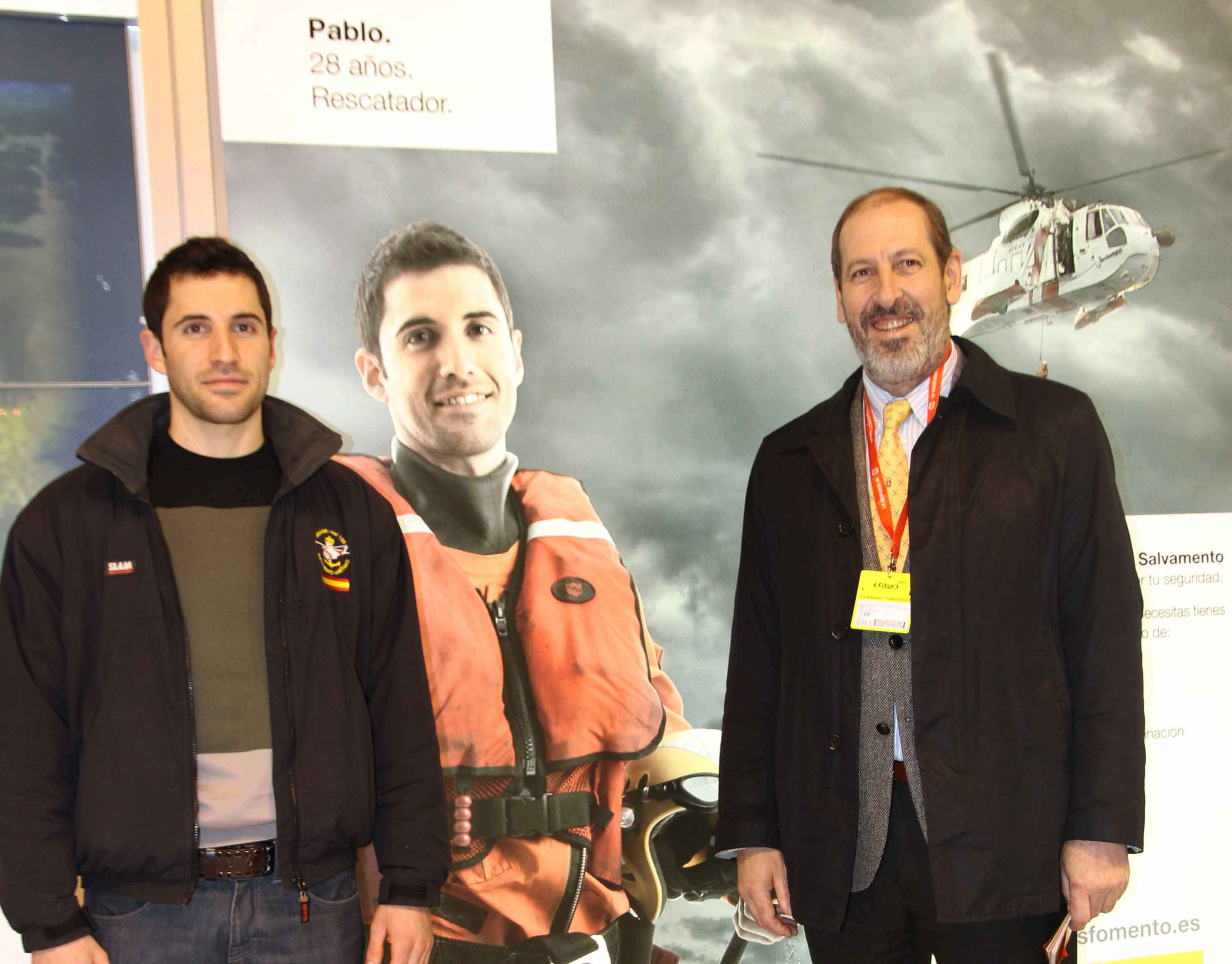 Dos hombres frente a un cartel de Salvamento Marítimo en el que el protagonista es uno de ellos dos.